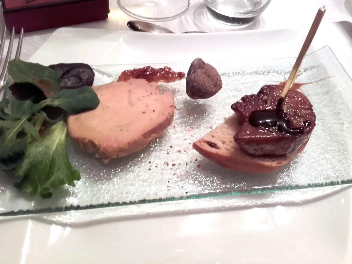 Une assiette sur une nappe blanche : une tranche de foie gras avec sa confiture, et un foie gras poêlé sur une tranche de pain grillé, quelques feuilles de salade.